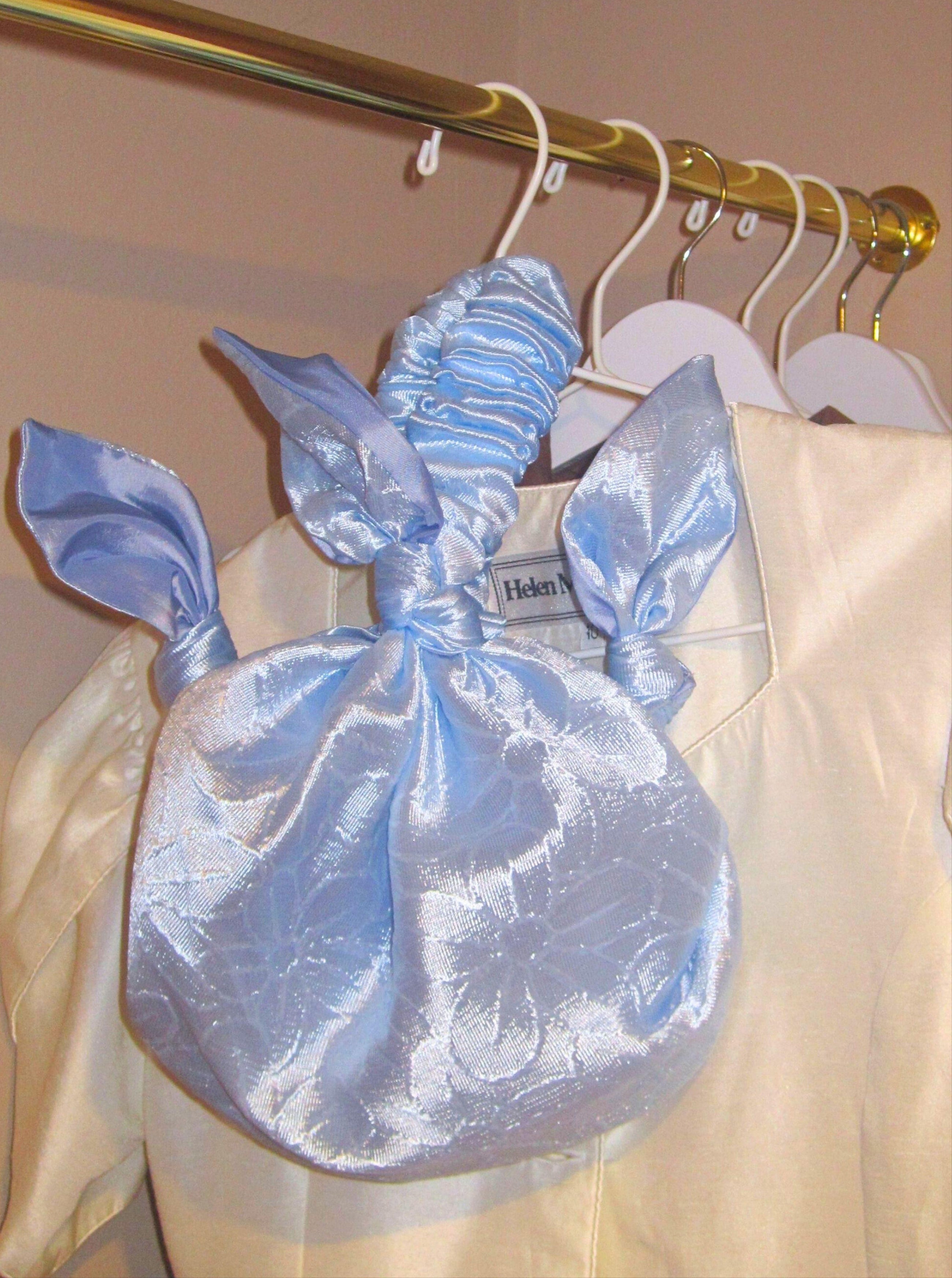 Light blue floral satin handbag hanging on a clothes rail with ivory garments in the back. Gold clothes rain, beige walls.