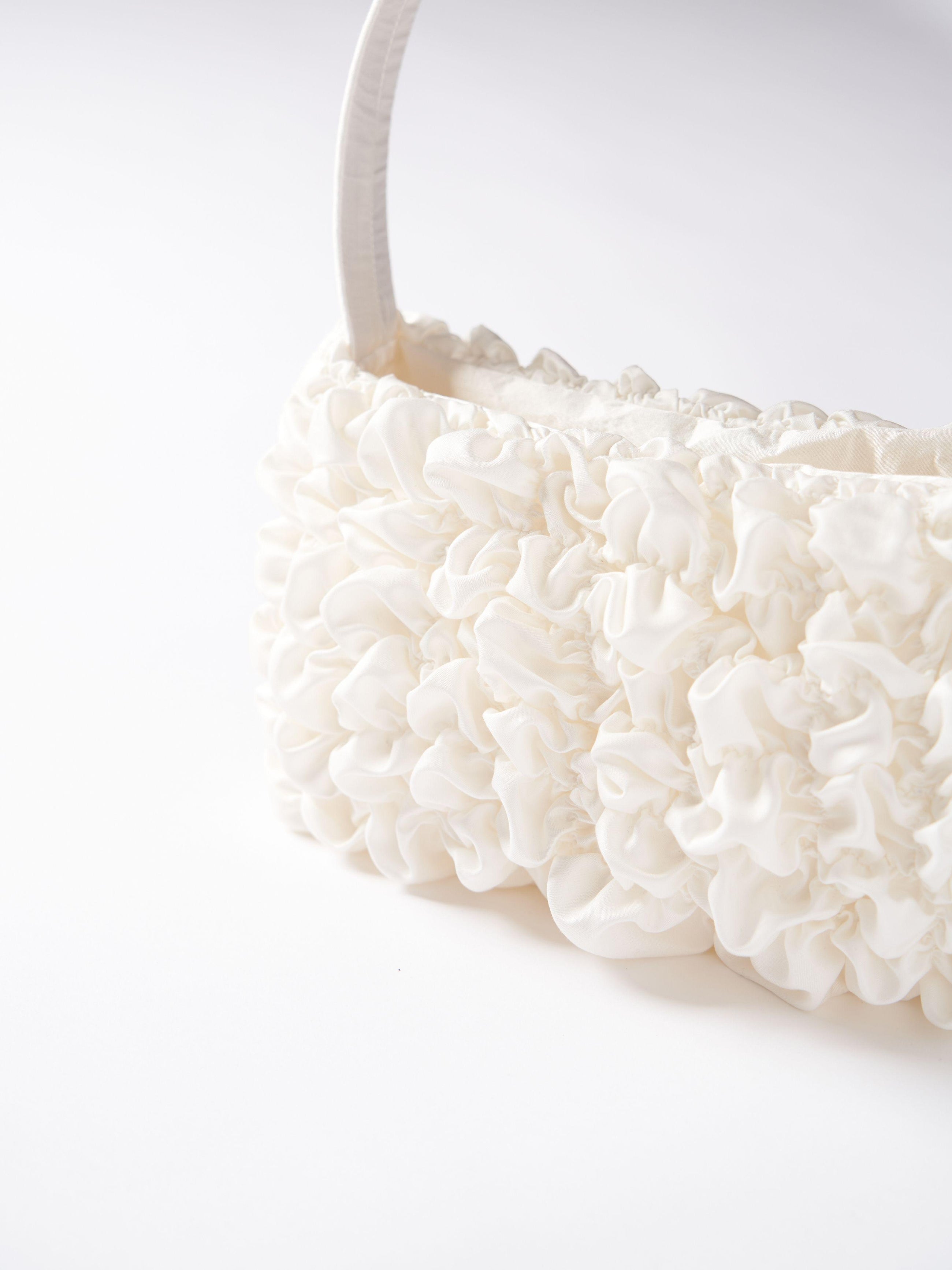 Close up of an ivory satin textured ruched front handbag. Set on a white background.
