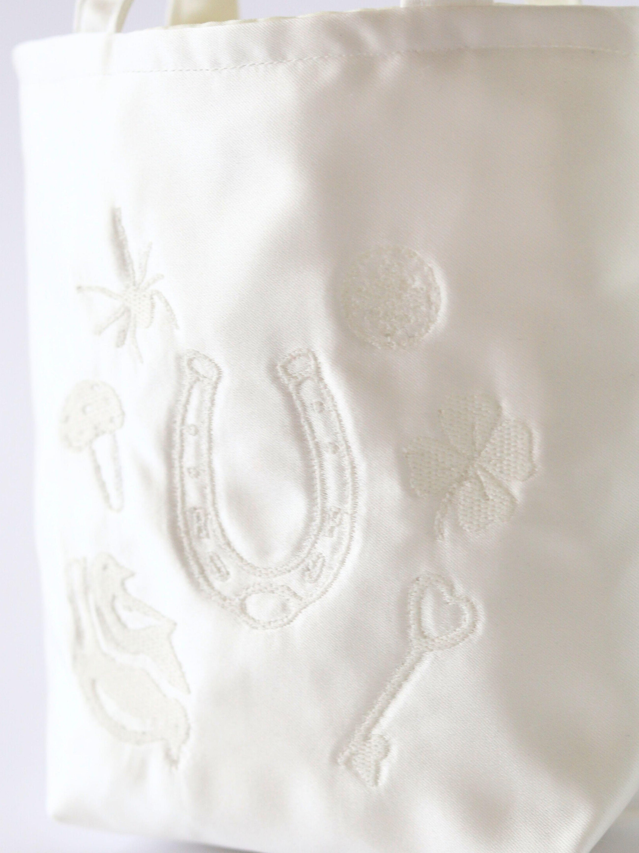 Close up of embroidered details on an iovery satin handbag. Good luck charms including a horseshoe, four leaf clover and toadstool.