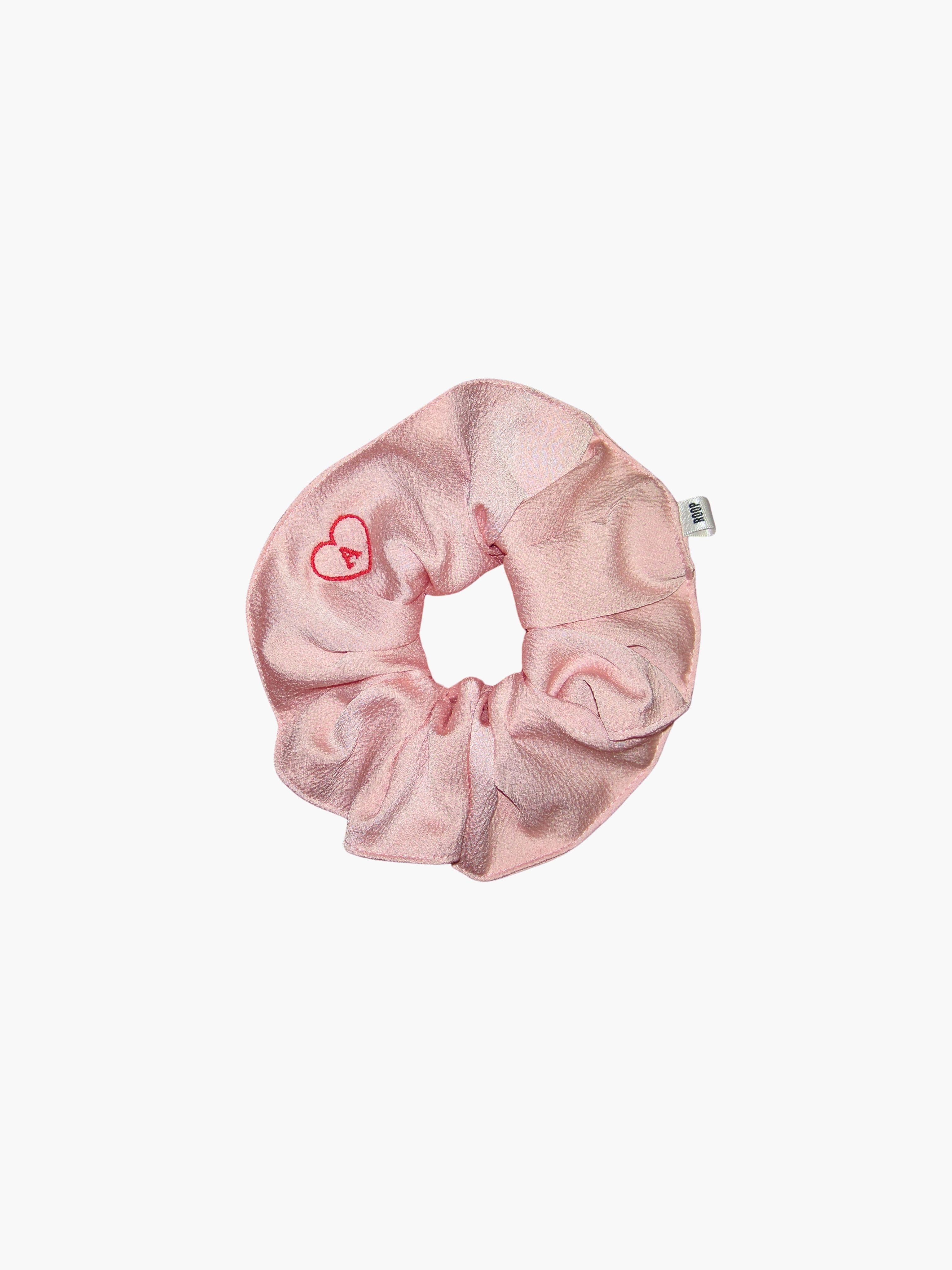 Pink satin scrunchie embroidered with a red heart with the letter A inside, set on a white background