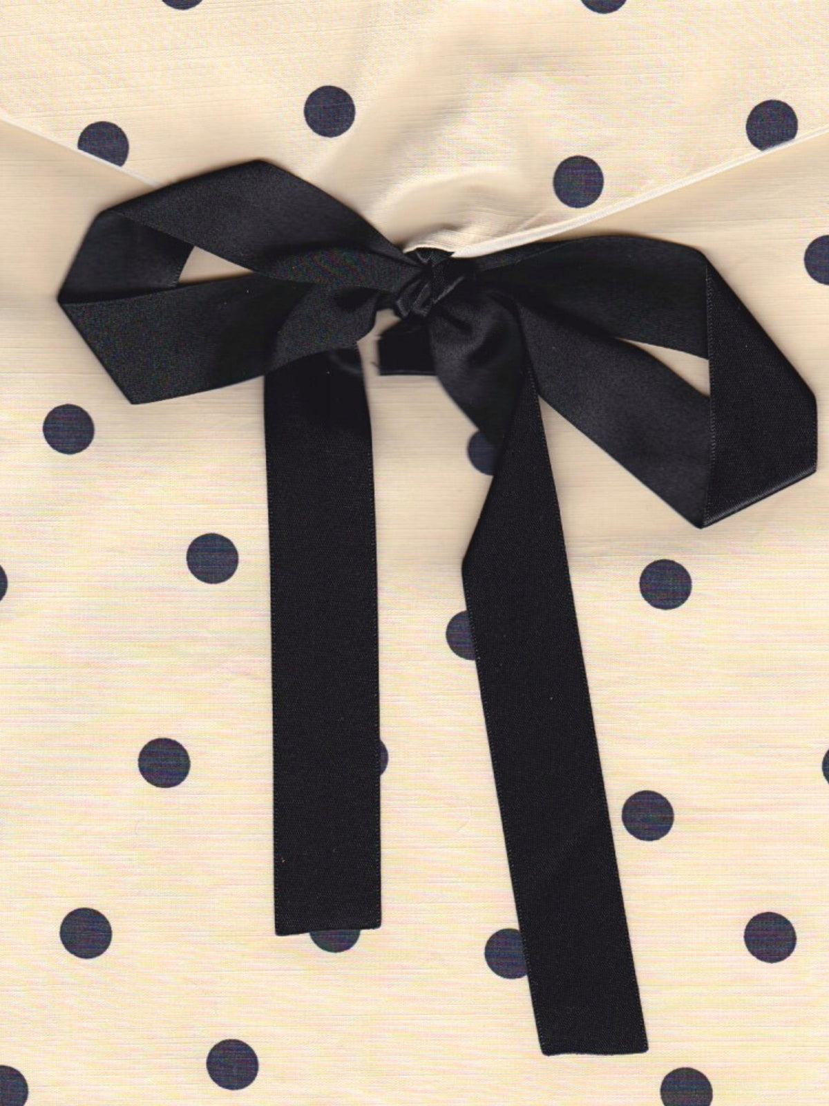Close up of a cream and black polka dot fabric pouch, tied with a black ribbon.