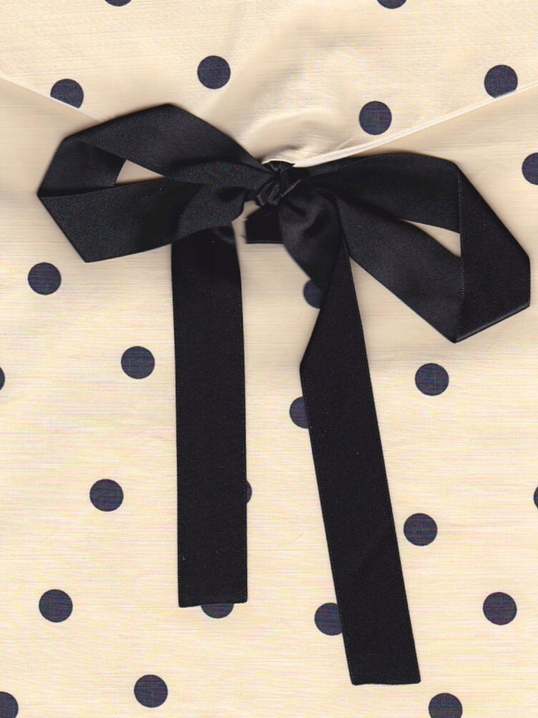 Close up of a cream and black polka dot fabric pouch, tied with a black ribbon.