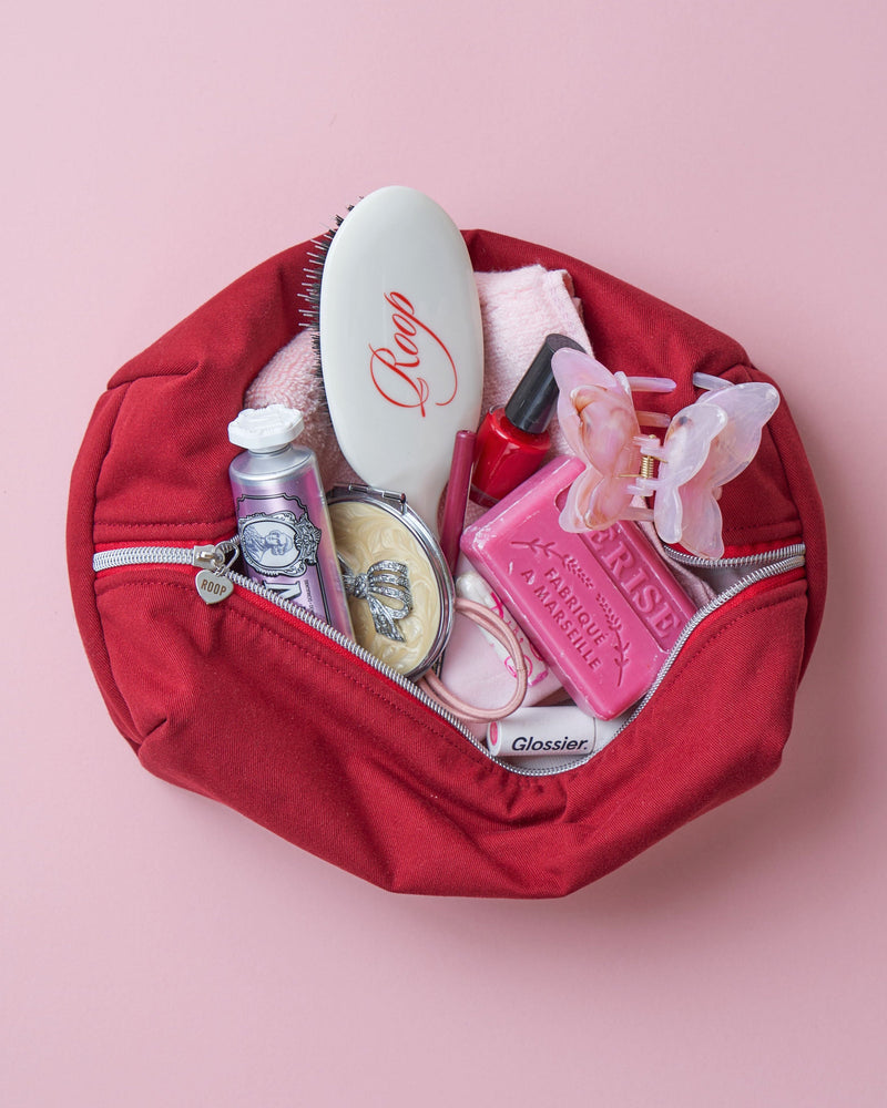 Burgundy cosmetic bag with various items on a pink background