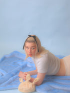 Person with a black bow in their hair lying on a blue faux fur blanket holding a cream knotted shaggy knotted handbag.