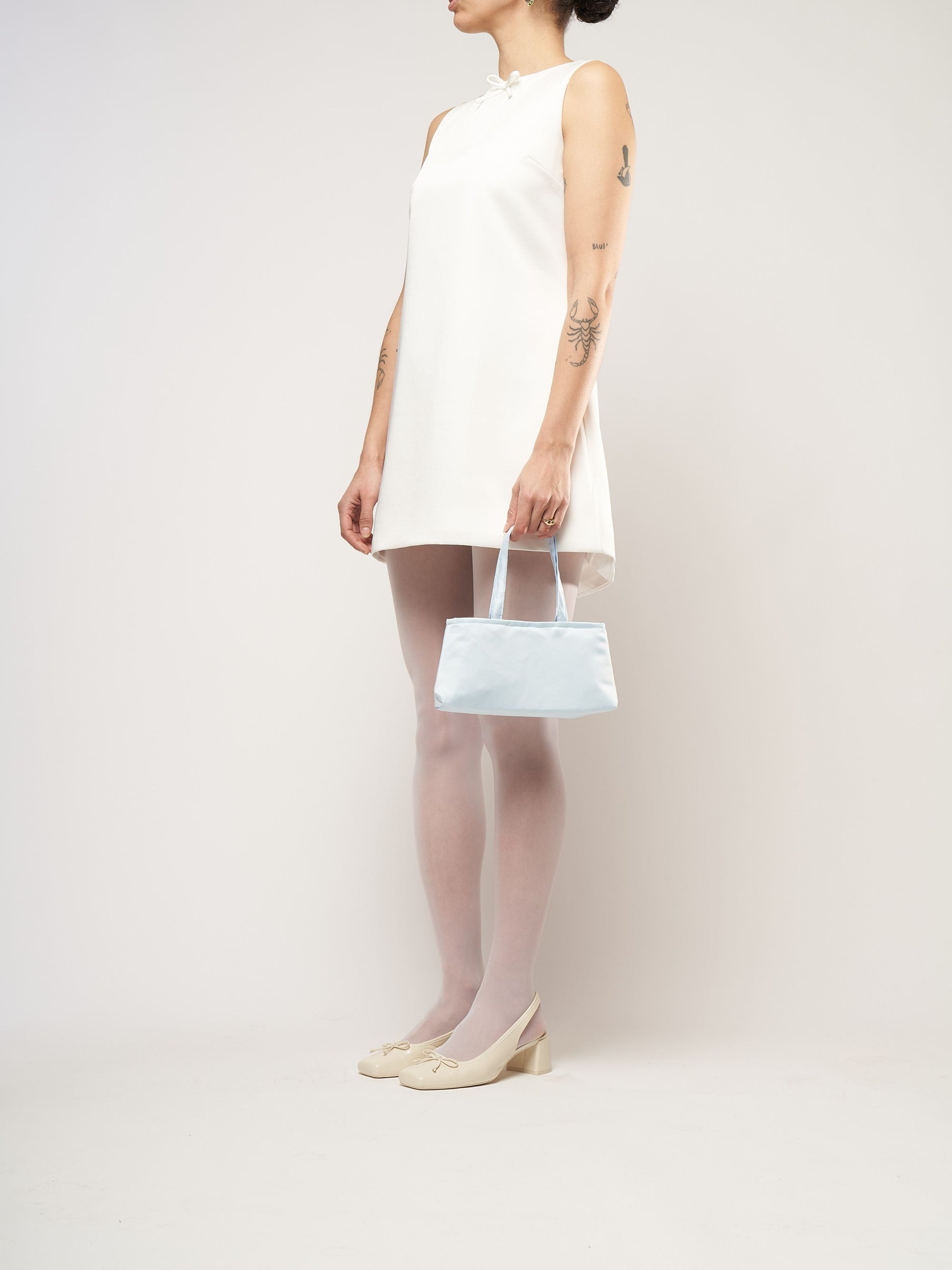 A model wearing a white mini bridal dress, holding a baby blue satin handbag.