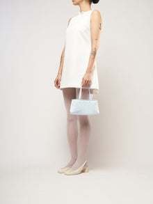 A model wearing a white mini bridal dress, holding a baby blue satin handbag.