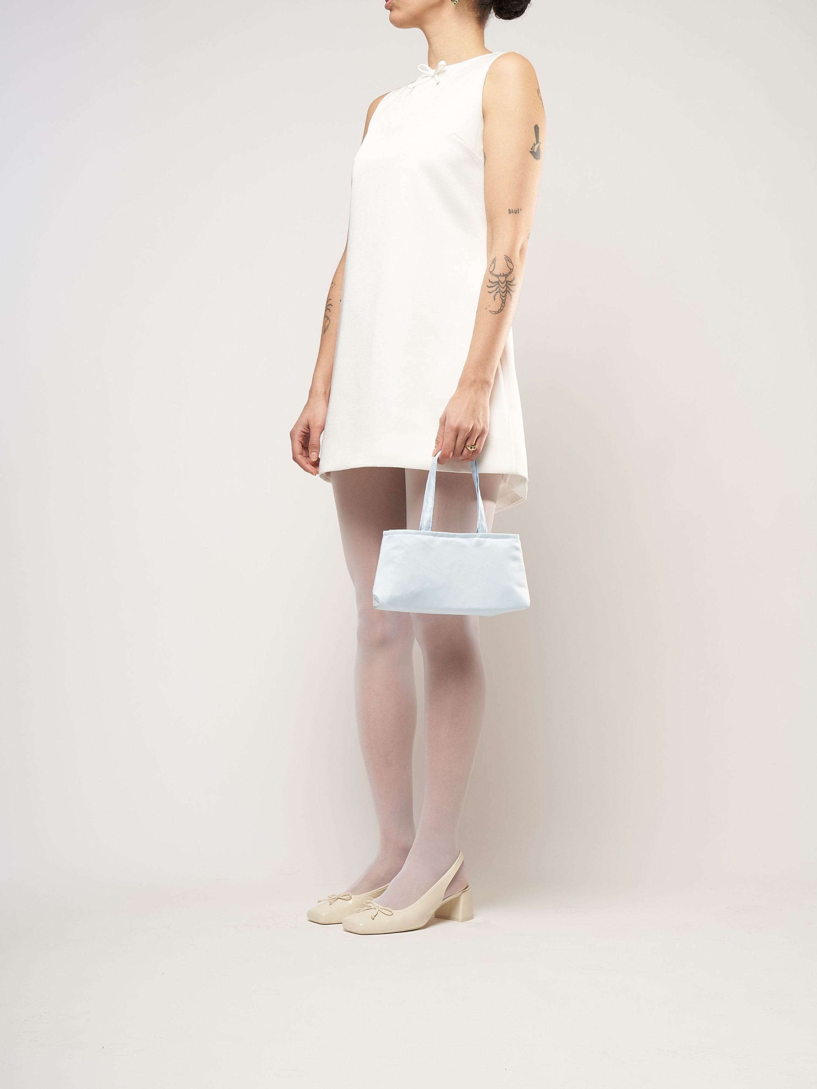 A model wearing a white mini bridal dress, holding a baby blue satin handbag.