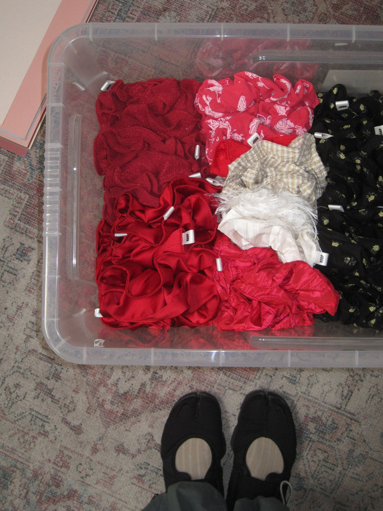 Clear plastic container filled with red, black and white scrunchies. Sat on a patterned carpet.