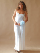 Person wearing an ivory satin slip dress, with a baby blue floral chiffon corsage around their wrist, set on a beige background