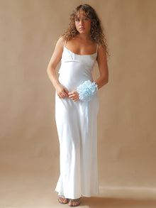 Person wearing an ivory satin slip dress, with a baby blue floral chiffon corsage around their wrist, set on a beige background