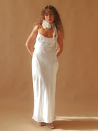 Person wearing an ivory satin slip dress with a white floral chiffon corsage around their neck, set on a beige background