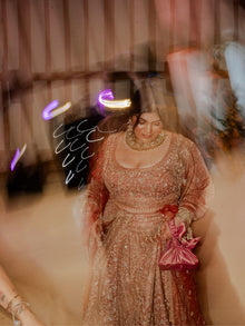 Woman in a traditional indian bridal outfit holds a pink handbag with a blurred background