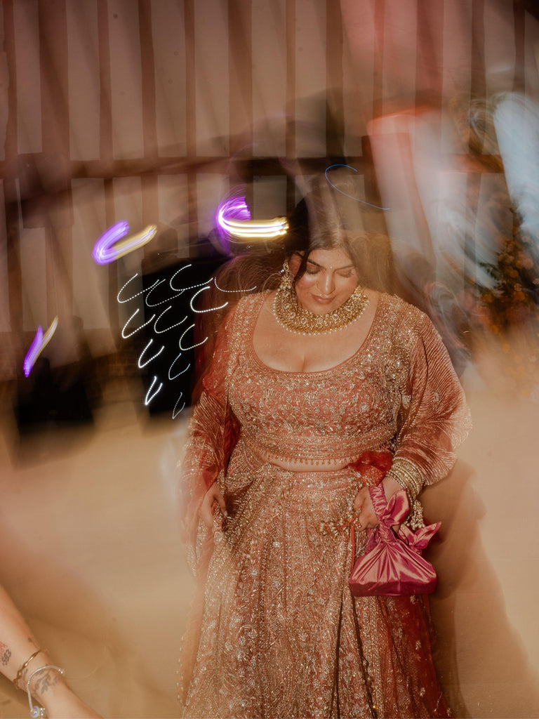 Woman in a traditional indian bridal outfit holds a pink handbag with a blurred background