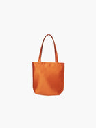 A burnt orange satin tote bag with. It features matching handles, set against a plain white background.