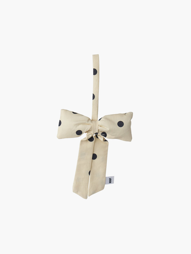 A cream and black polka dot padded fabric bow featuring a loop for hanging. The bow exudes a playful and decorative feel.
