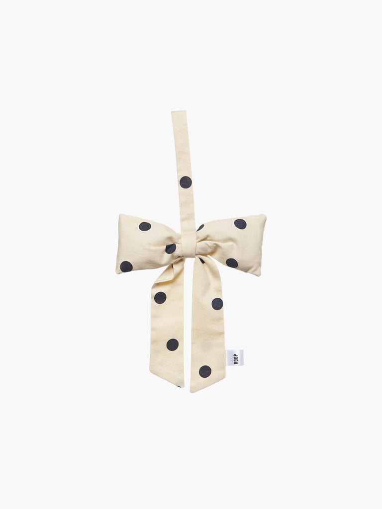 A cream and black polka dot padded fabric bow featuring a loop for hanging. The bow exudes a playful and decorative feel.