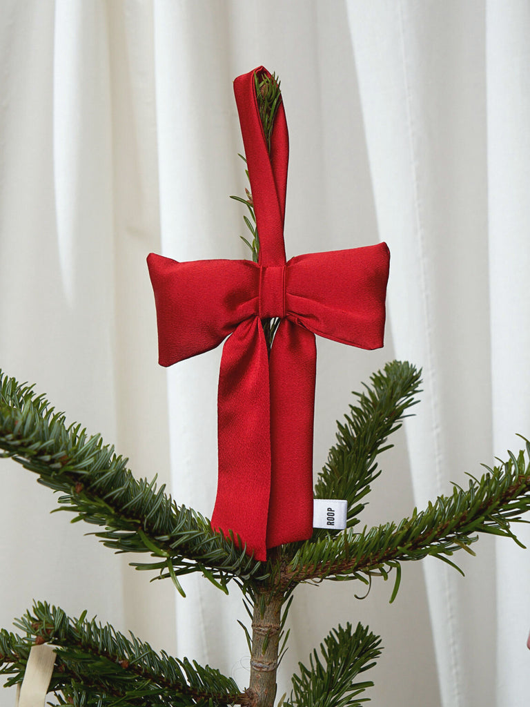 Red bow satin tree decoration on a Christmas tree branch with a white curtain background