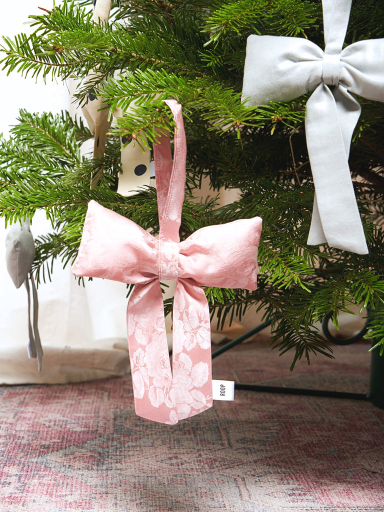 Pink floral satin decorative bow ornament on a Christmas tree with a silver bow in the background.
