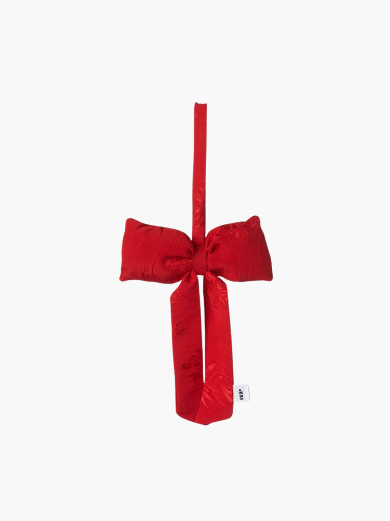 A red floral satin padded fabric bow featuring a loop for hanging. The bow exudes a playful and decorative feel.