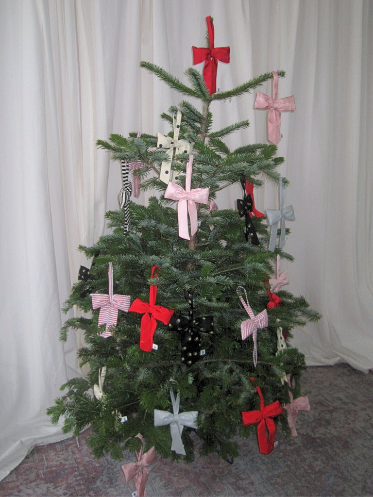 Decorated Christmas tree with various padded bow decorations against a white curtain background on a pink patterned rug.