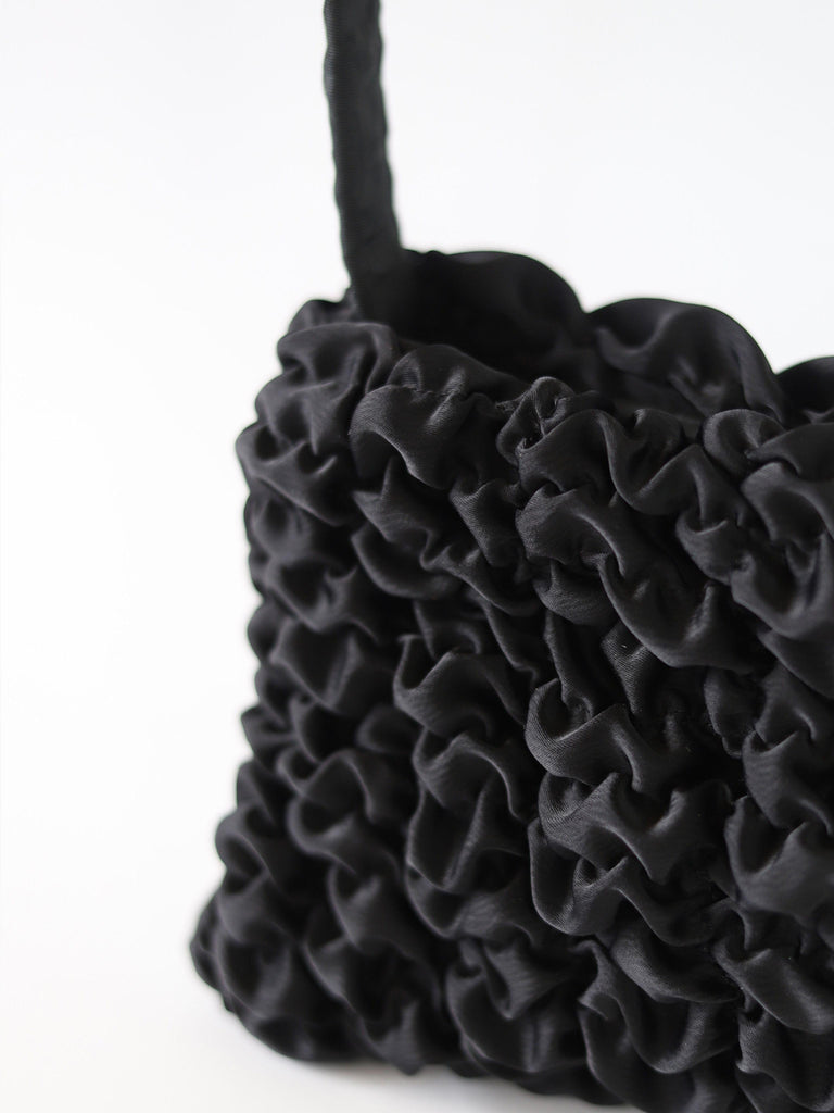 Close up of a black satin textured handbag on a white background