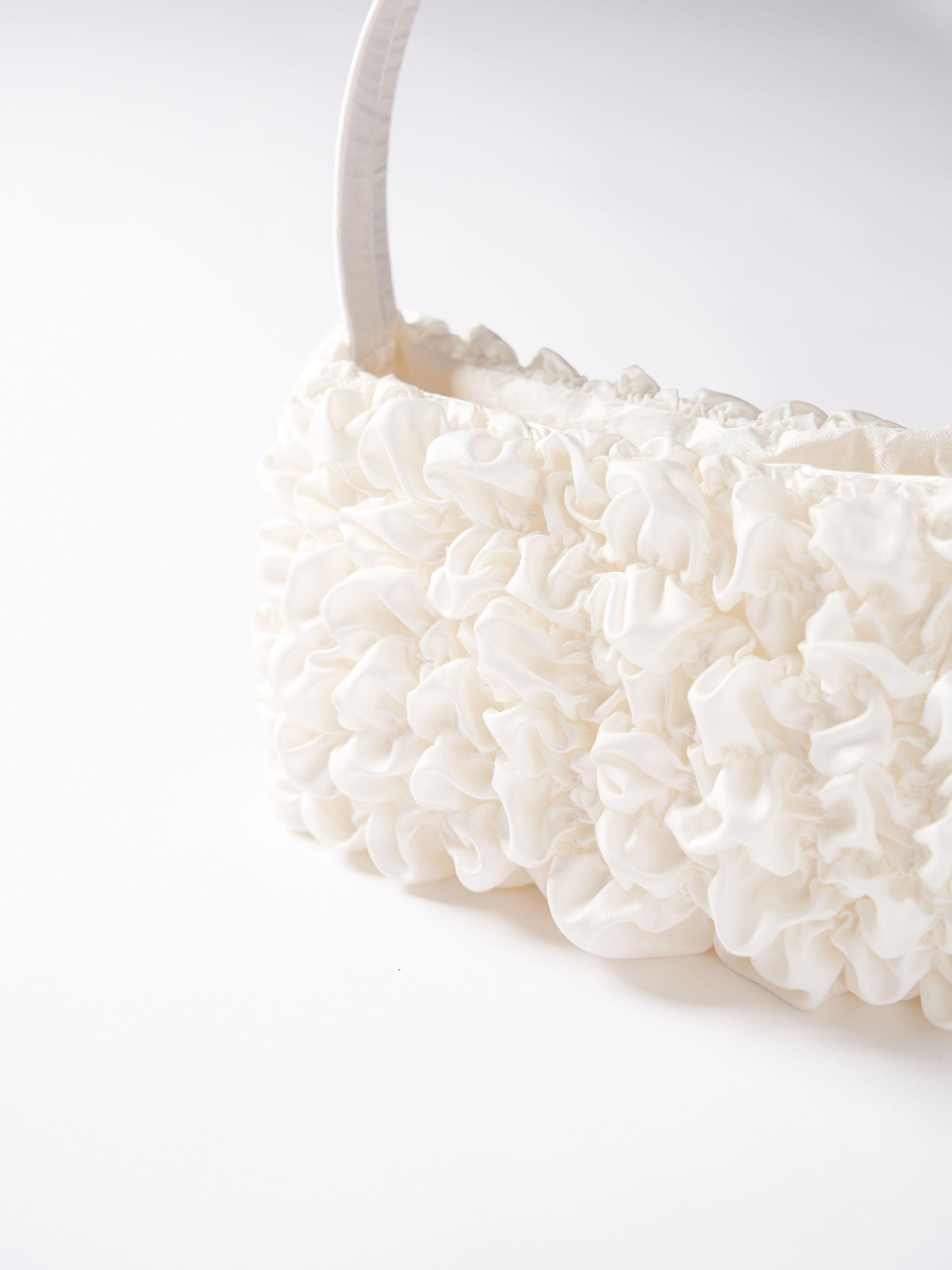 Close up of an ivory satin textured ruched front handbag. Set on a white background.