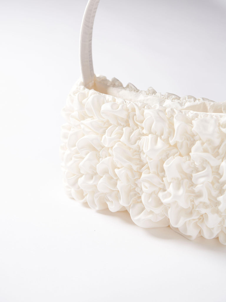 Close up of an ivory satin textured ruched front handbag. Set on a white background.