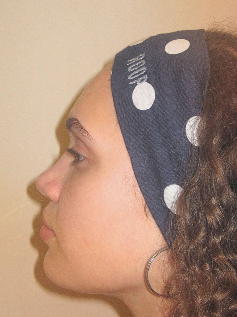 Side profile of a person wearing a navy blue stretch headband with white polka dots on a plain background