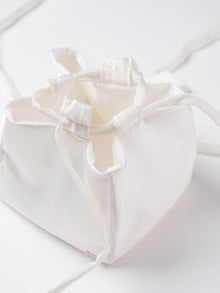 Close up of an ivory satin box drawstring handbag with ribbon drawstring details, open to reveal interior, set on a white background