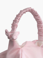 Close up of pink satin ruched handle handbag with decorative bows, set on a white background