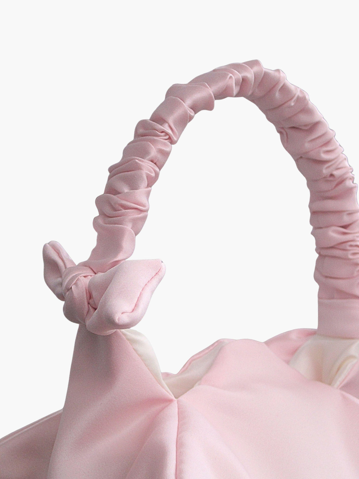 Close up of pink satin ruched handle handbag with decorative bows, set on a white background