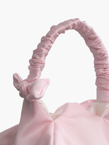 Close up of pink satin ruched handle handbag with decorative bows, set on a white background
