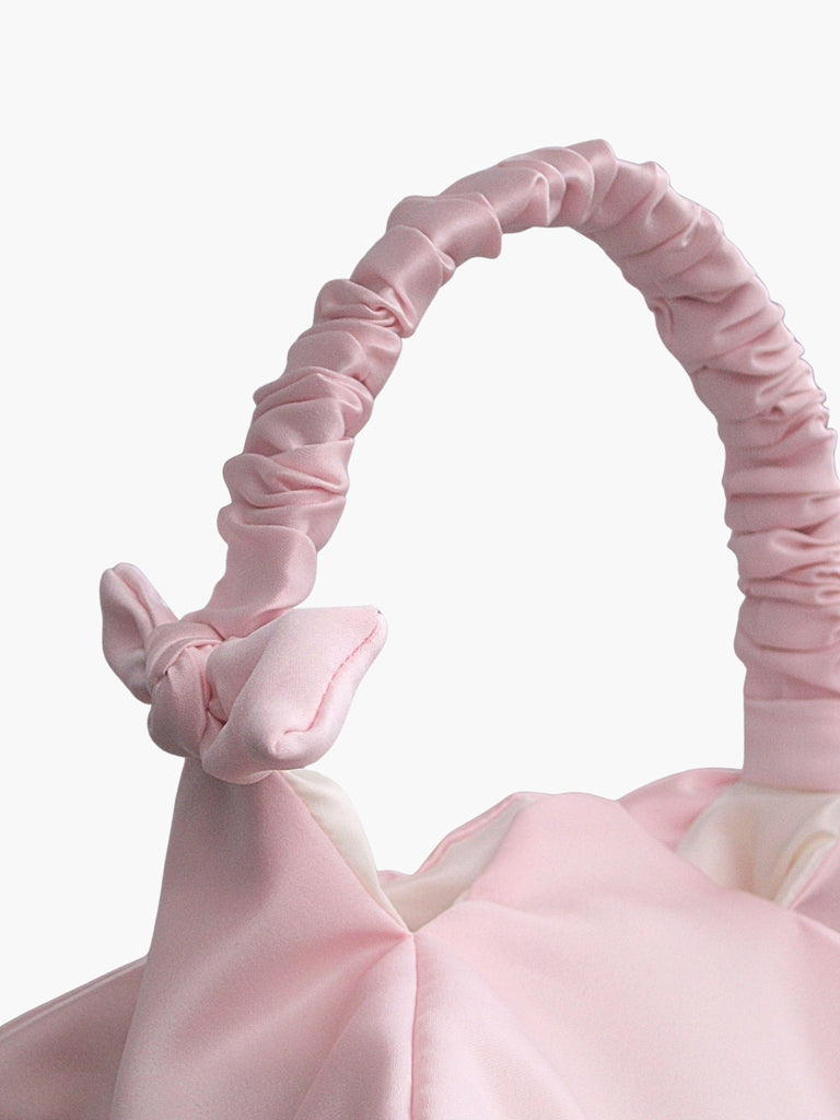 Close up of pink satin ruched handle handbag with decorative bows, set on a white background