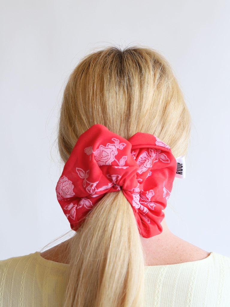Close up of a person with blonde hair wearing a red rose print mesh scrunchie against a white background
