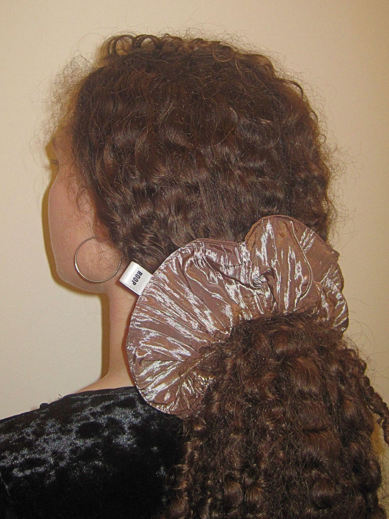 Person with brown curly hair wearing a large brown crinkle taffeta scrunchie,  set against a plain background