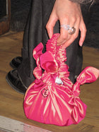 Pink knotted taffeta bag held by a person on a wooden floor. embroidered with a black heart with an L in the centre on the front.