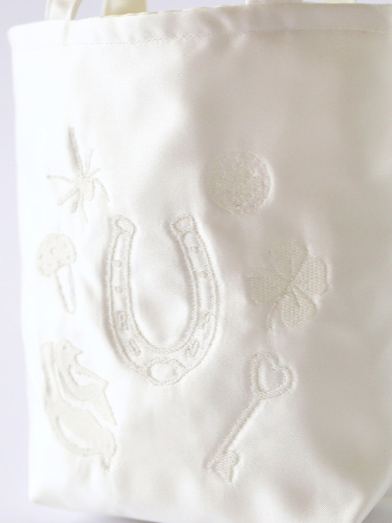 Close up of embroidered details on an iovery satin handbag. Good luck charms including a horseshoe, four leaf clover and toadstool.