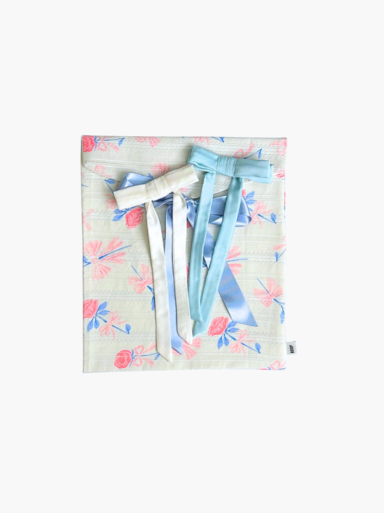 pair of satin hair clips, one baby blue, one ivory, sat on top of a floral patterned ribbon tied fabric git pouch, set against a white background