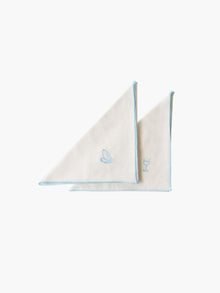 Two ivory cloth napkins with light blue hems and small embroidered designs: one with a cake and the other with a wine glass. Minimalist and elegant.