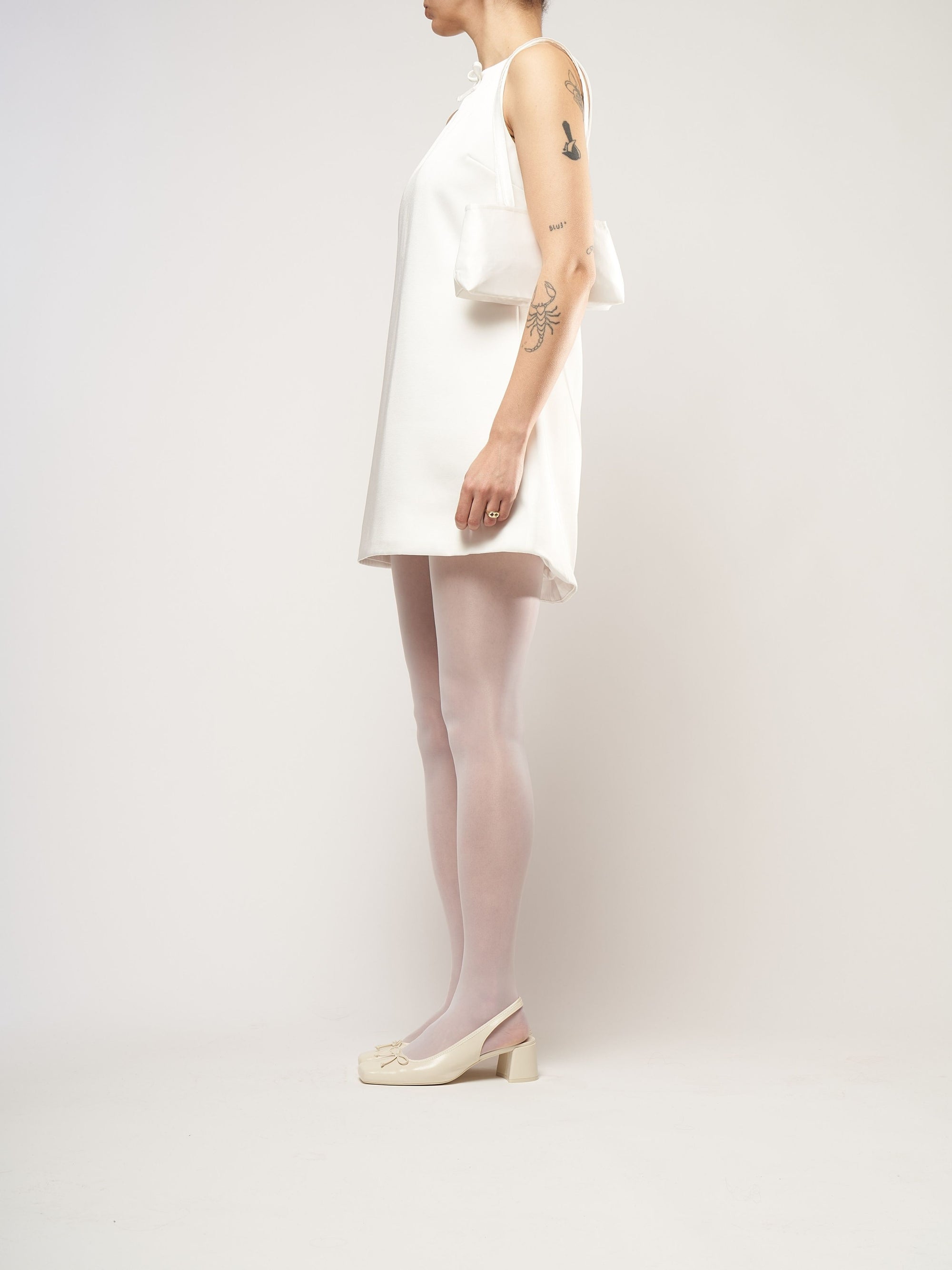 A model dressed in a white bridal mini dress, wearing an ivory satin baguette shape handbag.
