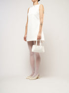 A model dressed in a white bridal mini dress, holding an ivory satin baguette shape handbag.