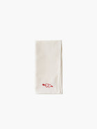 A folded cream-colored cloth napkin with a red embroidered heart design in the corner, set against a plain white background. Simple and elegant.