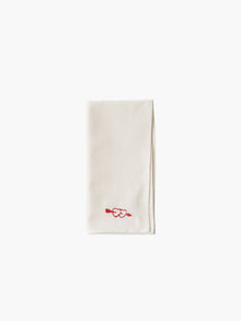 A folded cream-colored cloth napkin with a red embroidered heart design in the corner, set against a plain white background. Simple and elegant.
