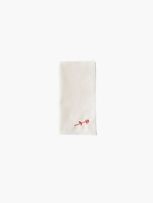 A folded cream-colored cloth napkin with a red embroidered rose design in the corner, set against a plain white background. Simple and elegant.