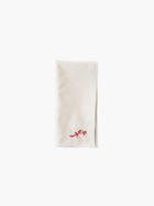 A folded cream-colored cloth napkin with a red embroidered rose design in the corner, set against a plain white background. Simple and elegant.
