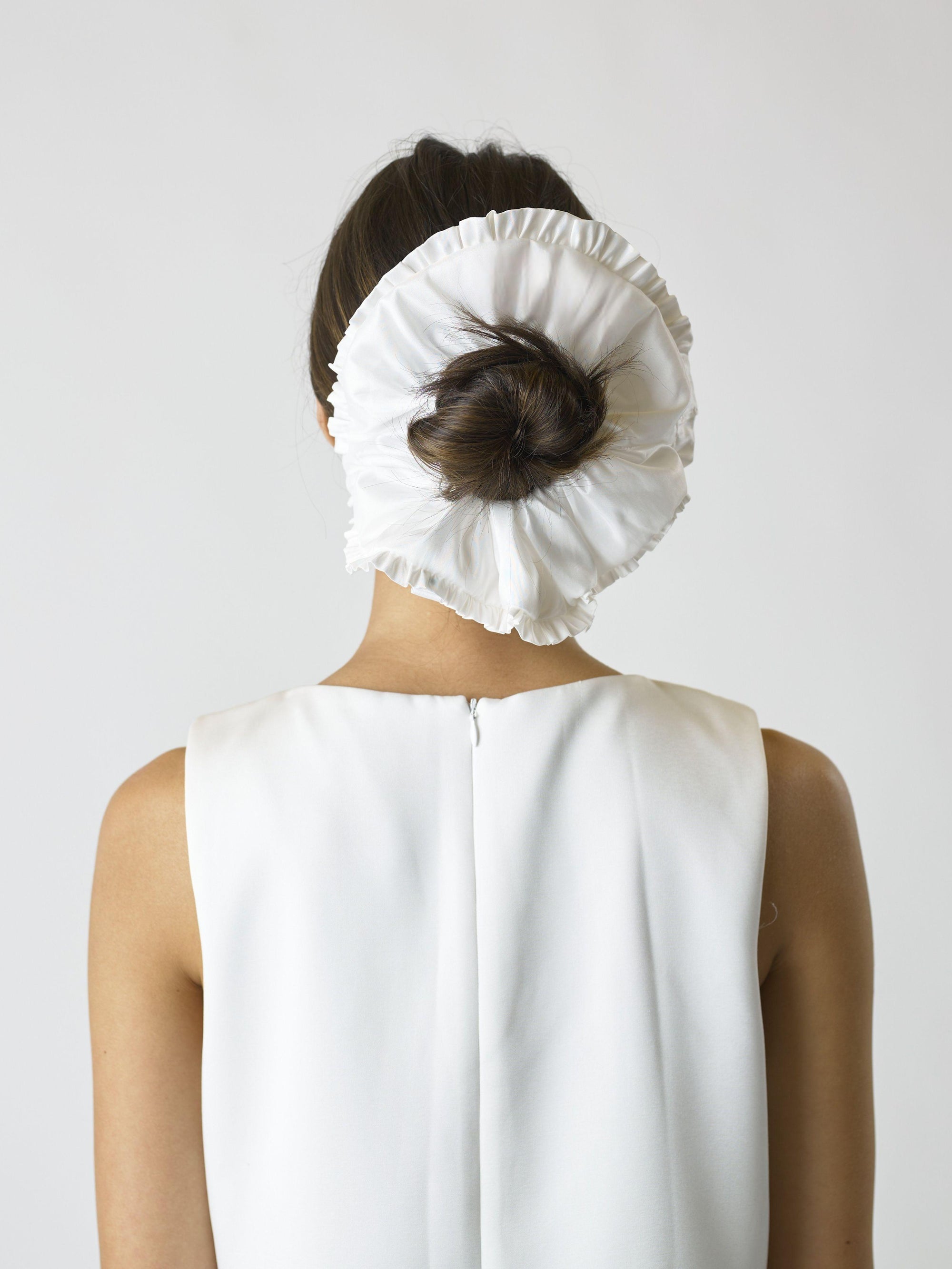 Person wearing an ivory large ruffled edge scrunchie over their bun, set against a plain background
