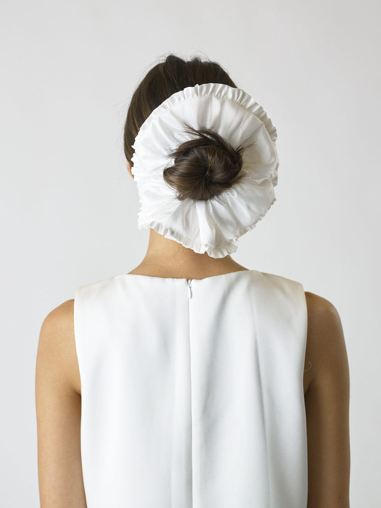 Person wearing an ivory large ruffled edge scrunchie over their bun, set against a plain background
