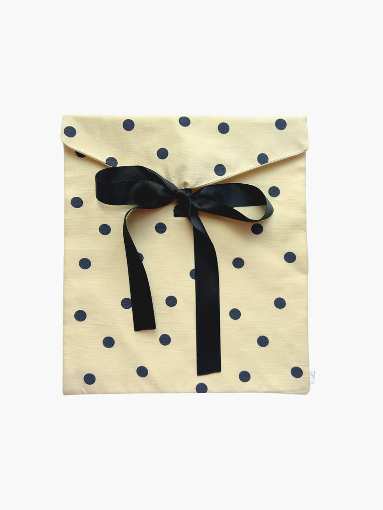Cream and black with polka dot patterned fabric envelope pouch tied with a black ribbon. Set on a white background.