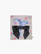 A floral print fabric gift pouch tied with a blue ribbon has a black satin hair bow scrunchie on top of it. Set on a white background.