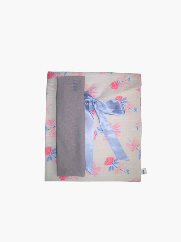 grey stretch headband, sat on top of a floral patterned ribbon tied fabric git pouch, set against a white background
